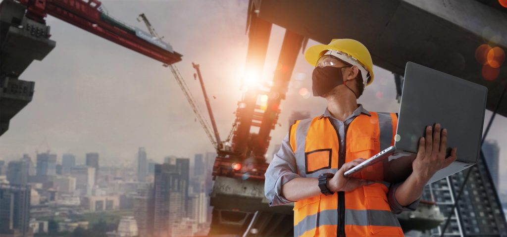 Hombre con chaleco reflectante, casco y portátil en medio de una obra 